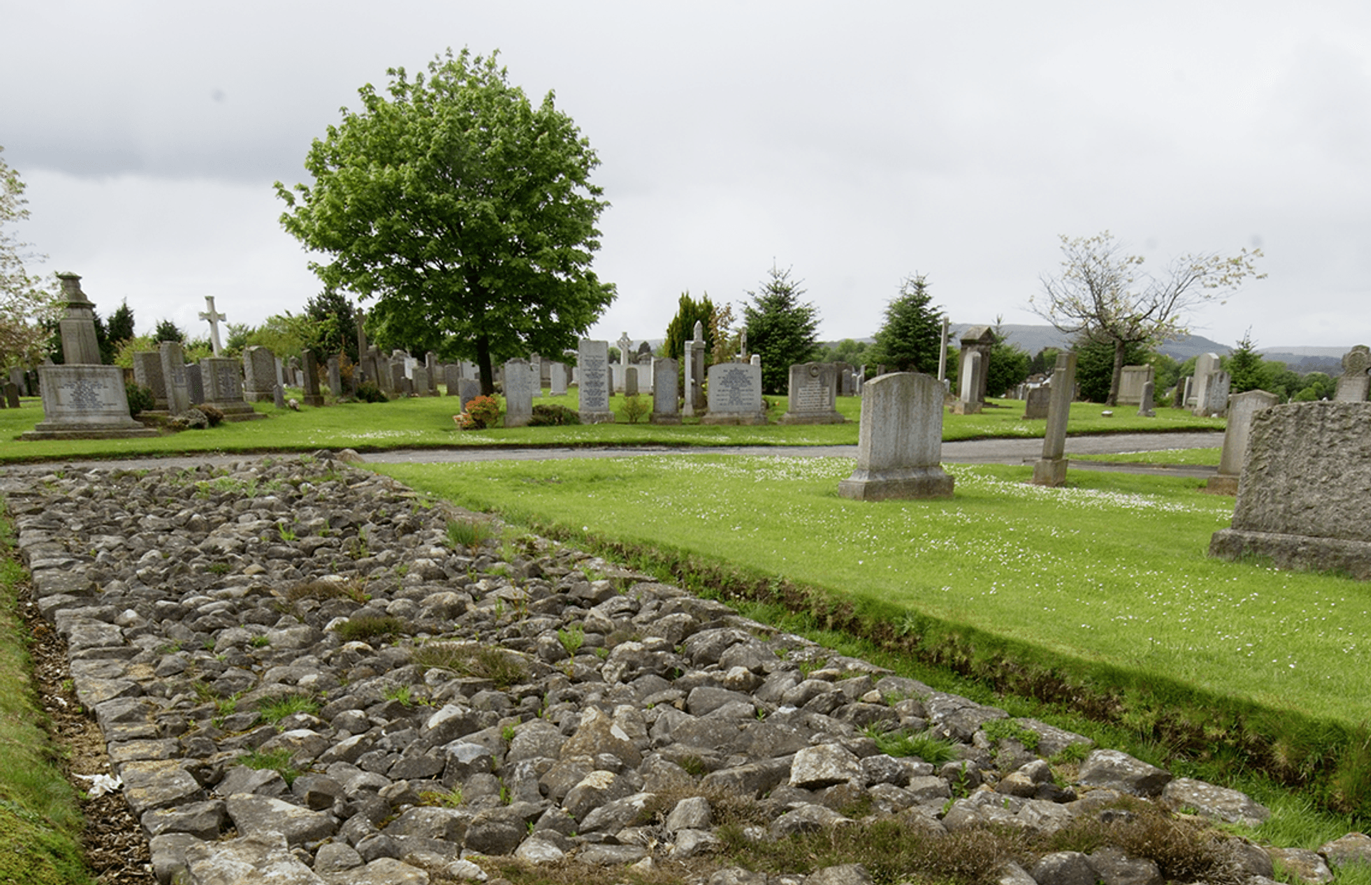 © Crown Copyright HES
New Kilpatrick Cemetery, the walls stone base. Rough cobbles in a rectangle surrounded by grass. Grave stones lie beyond it.
Reconstruction of Bearsden Camp with the wall stretching out to New Kilpatrick. © Crown Copyright HES
New Kilpatrick Cemetery, the walls stone base. Rough cobbles in a rectangle surrounded by grass. Grave stones lie beyond it.
Reconstruction of Bearsden Camp with the wall stretching out to New Kilpatrick.