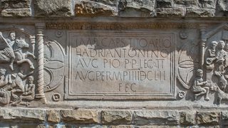 © Rediscovering the Antonine Wall Project
A sandstone distance stone built into a brick wall. The distance stone has a Latin inscription in its center, flanked on either side by carved images. © Rediscovering the Antonine Wall Project
A sandstone distance stone built into a brick wall. The distance stone has a Latin inscription in its center, flanked on either side by carved images.
