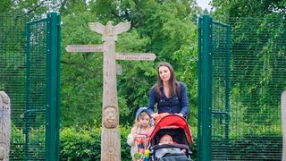 © Rediscovering the Antonine Wall Project.
A woman pushing a pram and accompanied by a child on a scooter enters through a green fenced gate. There is a wooden sculpture on either side of the group. © Rediscovering the Antonine Wall Project.
A woman pushing a pram and accompanied by a child on a scooter enters through a green fenced gate. There is a wooden sculpture on either side of the group.