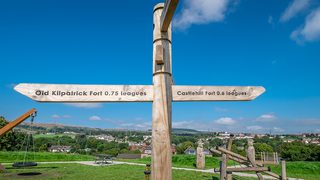 © Rediscovering the Antonine Wall Project
Duntocher Fort, Goldenhill Park. A wooden finger sign with the play park behind it on a sunny day. Trees and houses beyond. © Rediscovering the Antonine Wall Project
Duntocher Fort, Goldenhill Park. A wooden finger sign with the play park behind it on a sunny day. Trees and houses beyond.