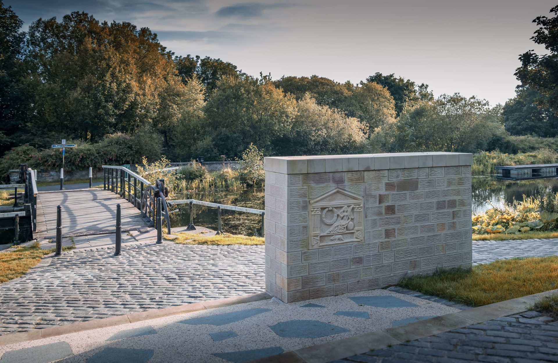 © Rediscovering the Antonine Wall Project
The Old Kilpatrick replica distance stone in a sandstone wall on a cobbled area in front of a canal bridge with trees beyond. © Rediscovering the Antonine Wall Project
The Old Kilpatrick replica distance stone in a sandstone wall on a cobbled area in front of a canal bridge with trees beyond.