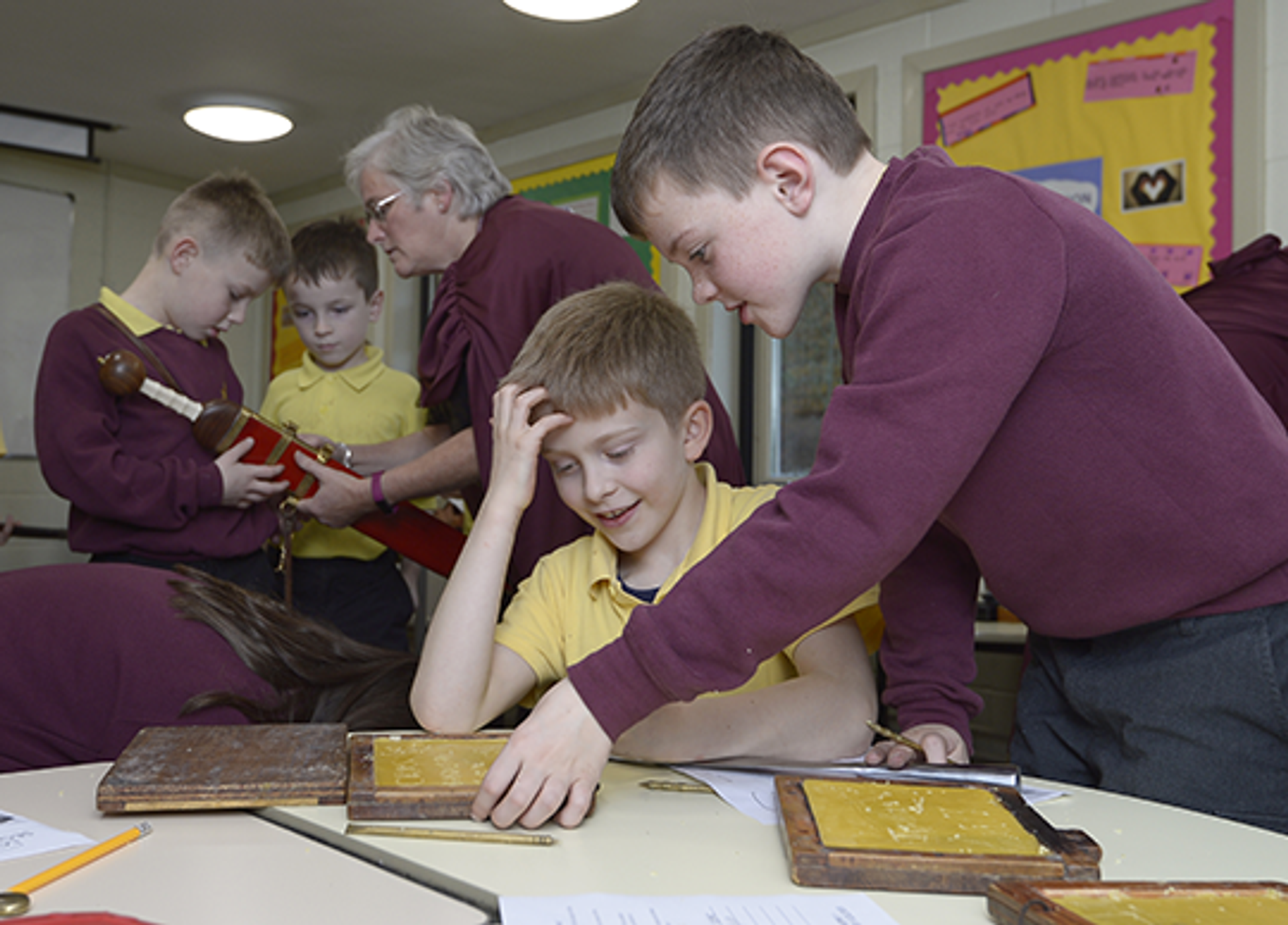 © Neil Hanna.
Two children at a classroom table using Roman replica items. A group of people in the background look at a Roman sword. © Neil Hanna.
Two children at a classroom table using Roman replica items. A group of people in the background look at a Roman sword.