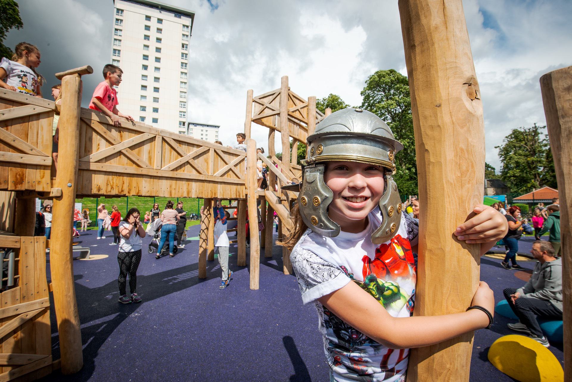 © Historic Environment Scotland
A Roman themed play park with wooden equipment on a sunny day. A smiling child in a white t shirt and a plastic Roman helmet. © Historic Environment Scotland
A Roman themed play park with wooden equipment on a sunny day. A smiling child in a white t shirt and a plastic Roman helmet.