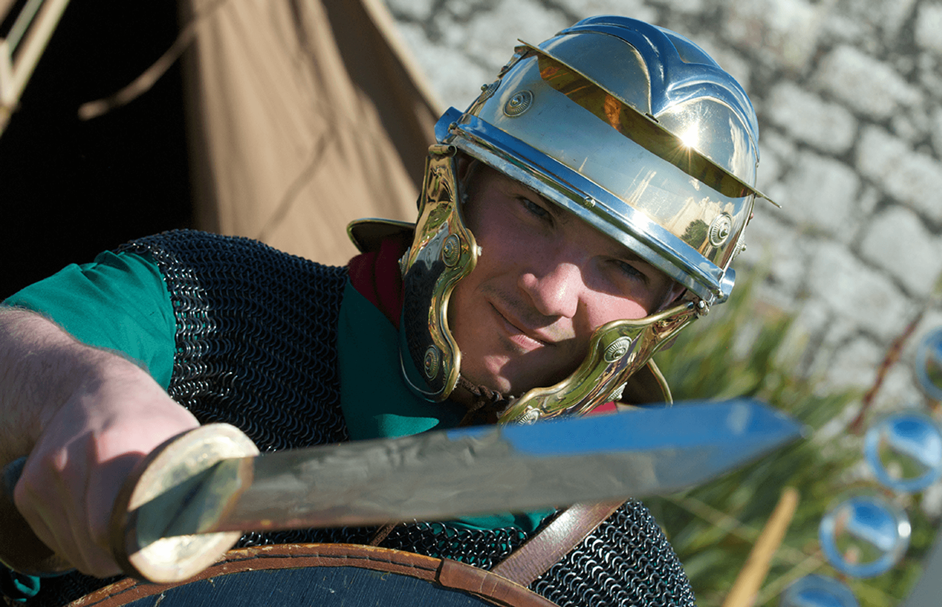 © Rob McDougall
A roman auxiliary soldier.
A Roman soldier in close up wears a metal helmet, green tunic, and chain mail. He holds a short sword, and an oval shield. © Rob McDougall
A roman auxiliary soldier.
A Roman soldier in close up wears a metal helmet, green tunic, and chain mail. He holds a short sword, and an oval shield.