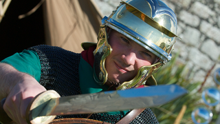 © Rob McDougall
A roman auxiliary soldier.
A Roman soldier in close up wears a metal helmet, green tunic, and chain mail. He holds a short sword, and an oval shield. © Rob McDougall
A roman auxiliary soldier.
A Roman soldier in close up wears a metal helmet, green tunic, and chain mail. He holds a short sword, and an oval shield.