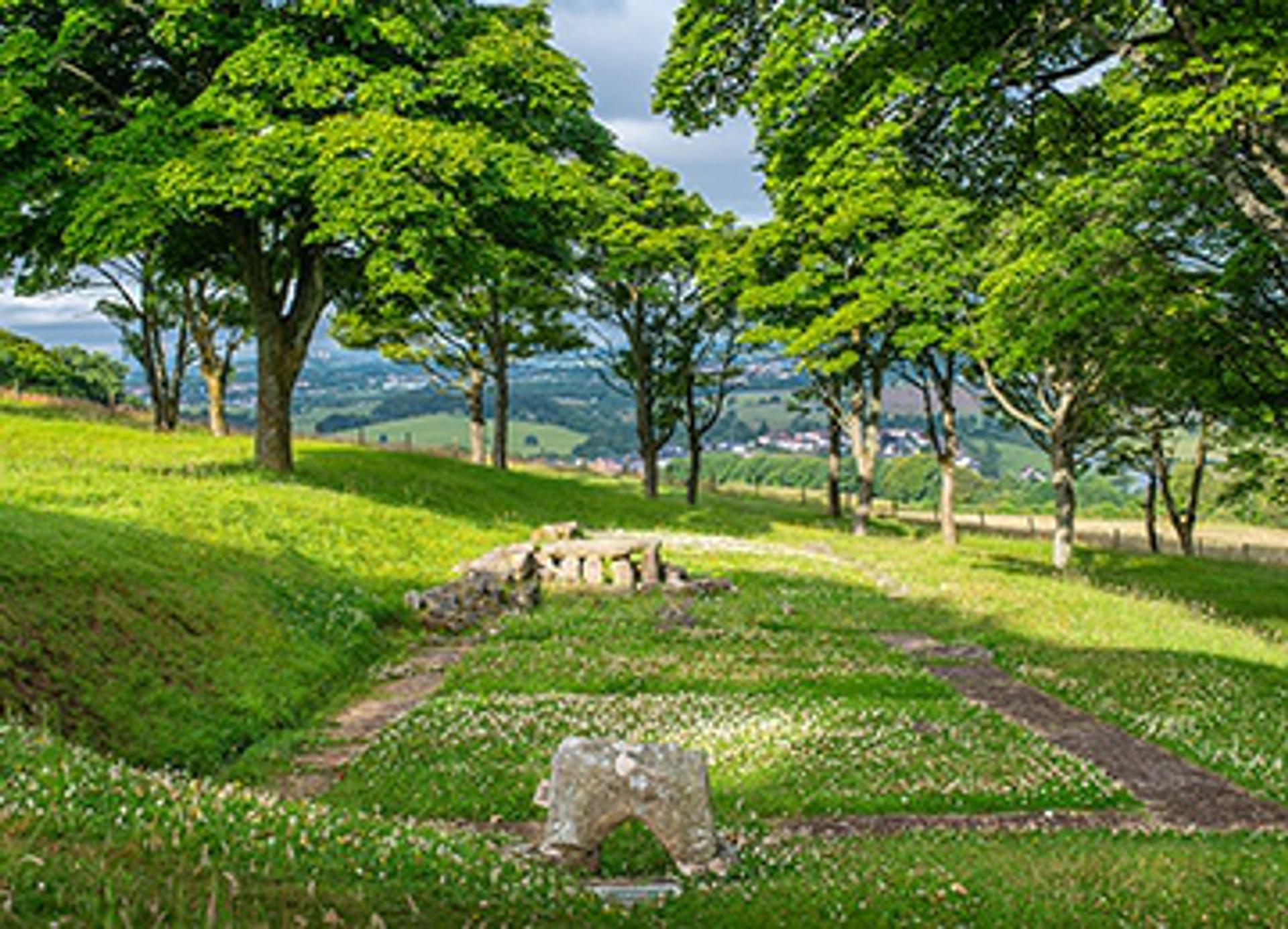 © Rediscovering the Antonine Wall Project
The square foundations of Bar Hill Roman bath house on a grassy hillside with trees. A section of low wall and underfloor heating system are visible. © Rediscovering the Antonine Wall Project
The square foundations of Bar Hill Roman bath house on a grassy hillside with trees. A section of low wall and underfloor heating system are visible.