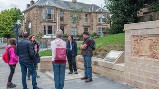 © Rediscovering the Antonine Wall Project
People stand next to the Falkirk replica Distance Slab. There is a low sandstone wall and an interpretation panel. © Rediscovering the Antonine Wall Project
People stand next to the Falkirk replica Distance Slab. There is a low sandstone wall and an interpretation panel.