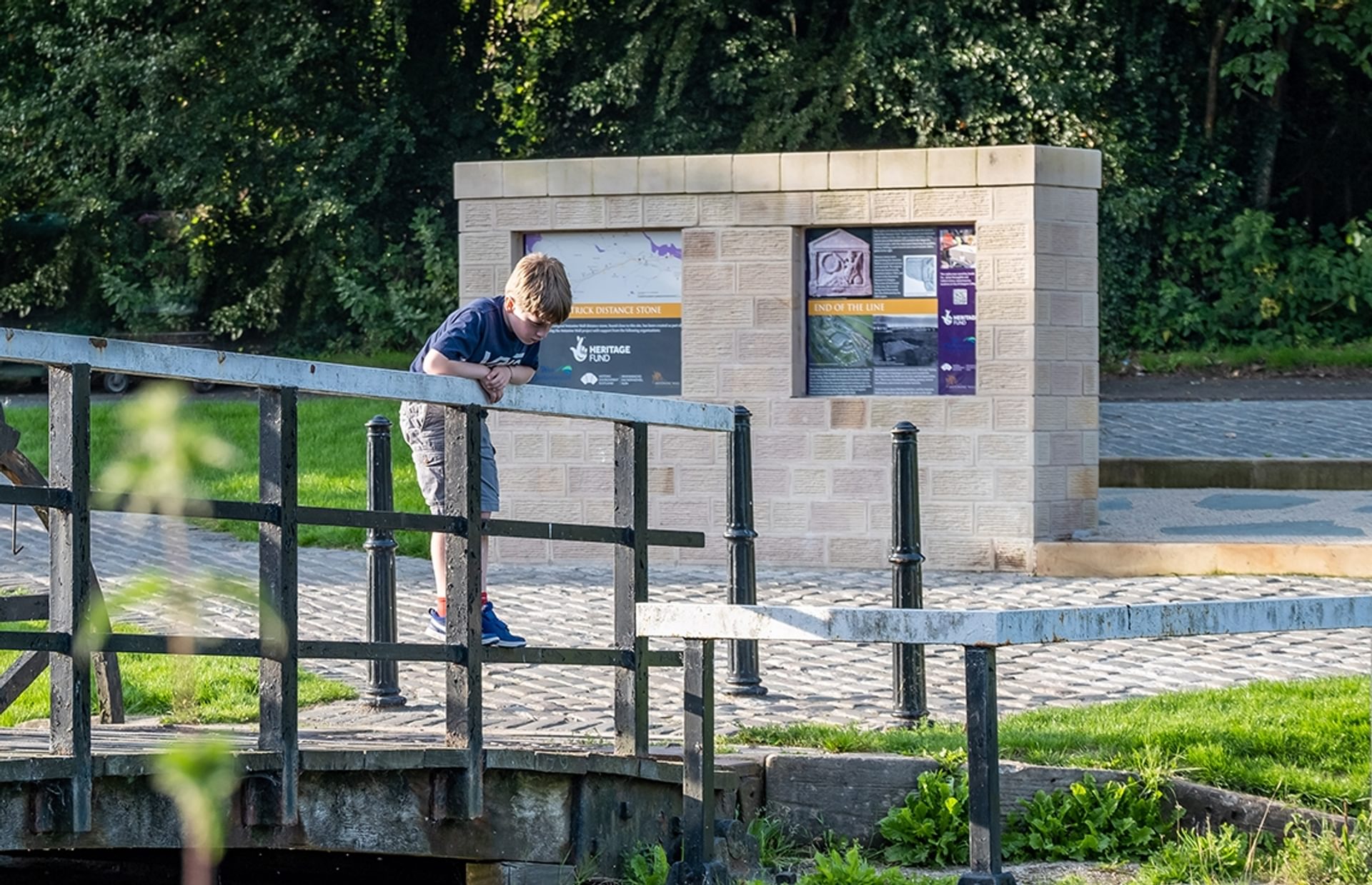 © Rediscovering the Antonine Wall Project
Old Kilpatrick, a boy stands on a bridge looking at the canal below him. The replica distance stone and trees behind him. © Rediscovering the Antonine Wall Project
Old Kilpatrick, a boy stands on a bridge looking at the canal below him. The replica distance stone and trees behind him.