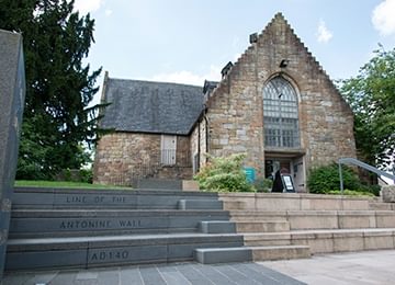 © Crown Copyright HES
Auld Kirk Museum, a set of concrete and grey stone steps go up to it with ‘Line of the Antonine Wall AD 140’ decorating them. © Crown Copyright HES
Auld Kirk Museum, a set of concrete and grey stone steps go up to it with ‘Line of the Antonine Wall AD 140’ decorating them.