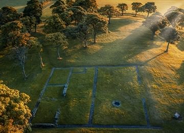 © Rediscovering the Antonine Wall Project
Bar Hill fort from above, a rectangular building and circular stone well visible in the grass. There are trees all around. © Rediscovering the Antonine Wall Project
Bar Hill fort from above, a rectangular building and circular stone well visible in the grass. There are trees all around.
