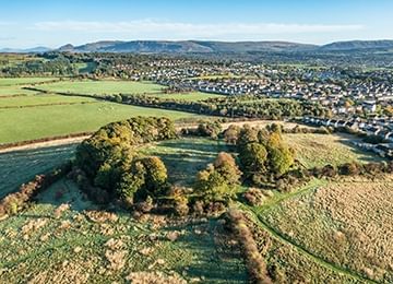 © Rediscovering the Antonine Wall Project
Castlehill, a wooded hill surrounded by farmland. There are streets to the right and blue sky and rolling hills behind. © Rediscovering the Antonine Wall Project
Castlehill, a wooded hill surrounded by farmland. There are streets to the right and blue sky and rolling hills behind.