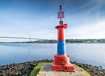 © Rediscovering the Antonine Wall Project
The River Clyde at Old Kilpatrick. A blue and red metal sculpture on a stone plinth, and a gravel beach in the foreground. © Rediscovering the Antonine Wall Project
The River Clyde at Old Kilpatrick. A blue and red metal sculpture on a stone plinth, and a gravel beach in the foreground.